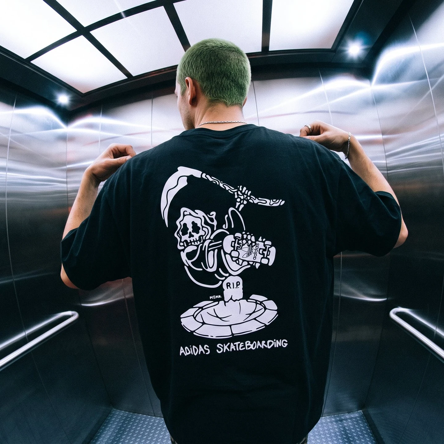 Person in an elevator wearing the black adidas Skateboarding tee — Ride in Peace grim reaper riding a board over an R.I.P. tombstone, MEKA. signature