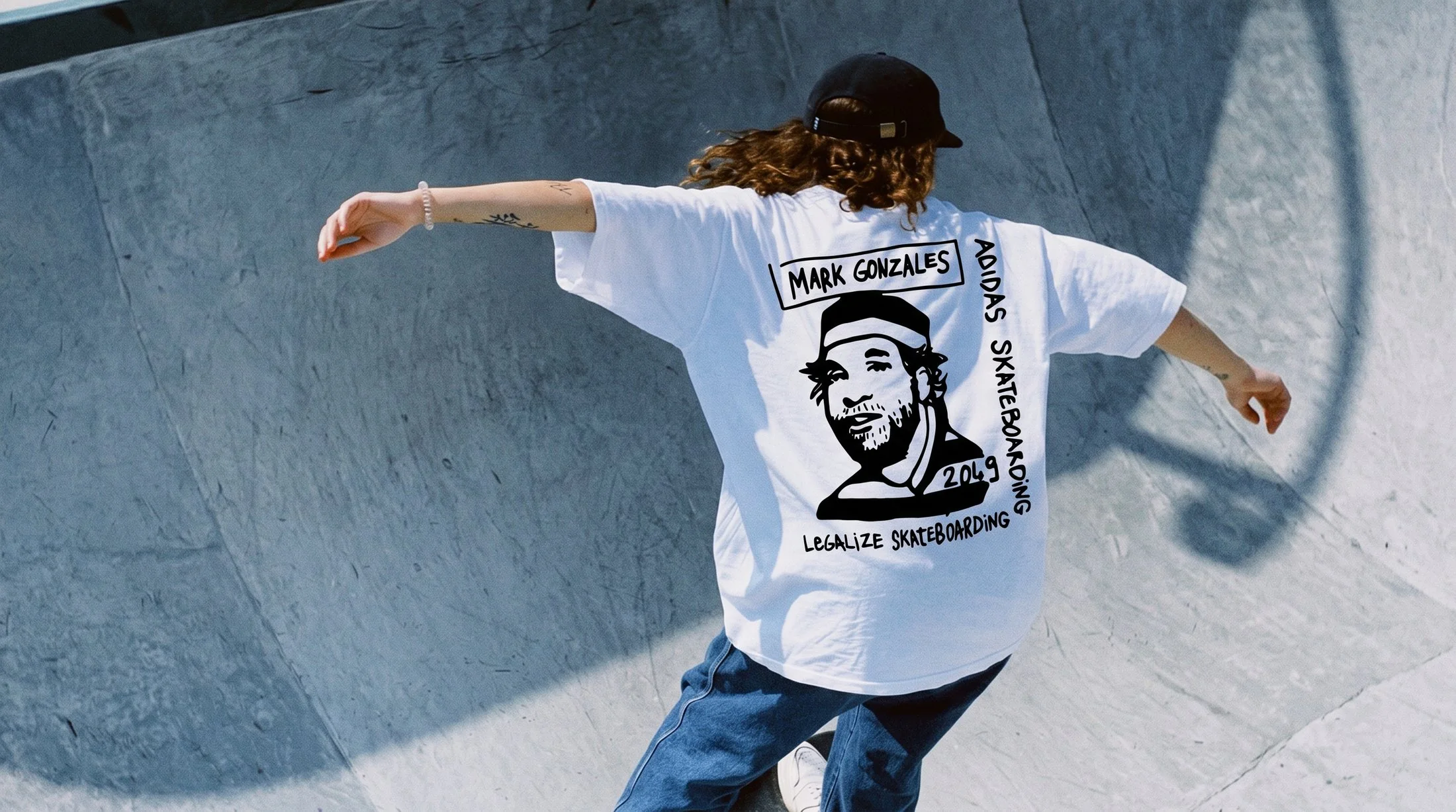 Skater riding a concrete bowl in the white Mark Gonzales adidas Skateboarding tee — Legalize Skateboarding hand-lettered graphic across the back
