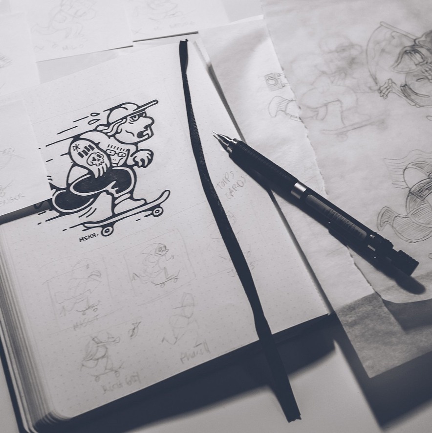 The sketchbook open on the desk, pen resting on the page