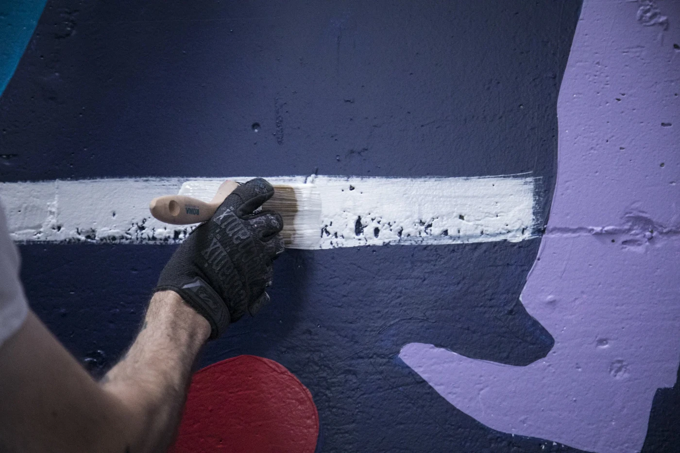 Close-up: gloved hand pulling the white line across the mural