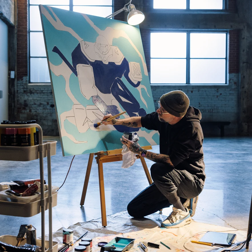 Kneeling at the canvas on the studio floor, blocking in the turquoise field around the figure