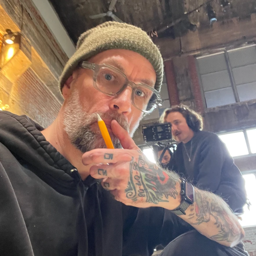 The artist on set, pencil in hand, camera crew working behind him