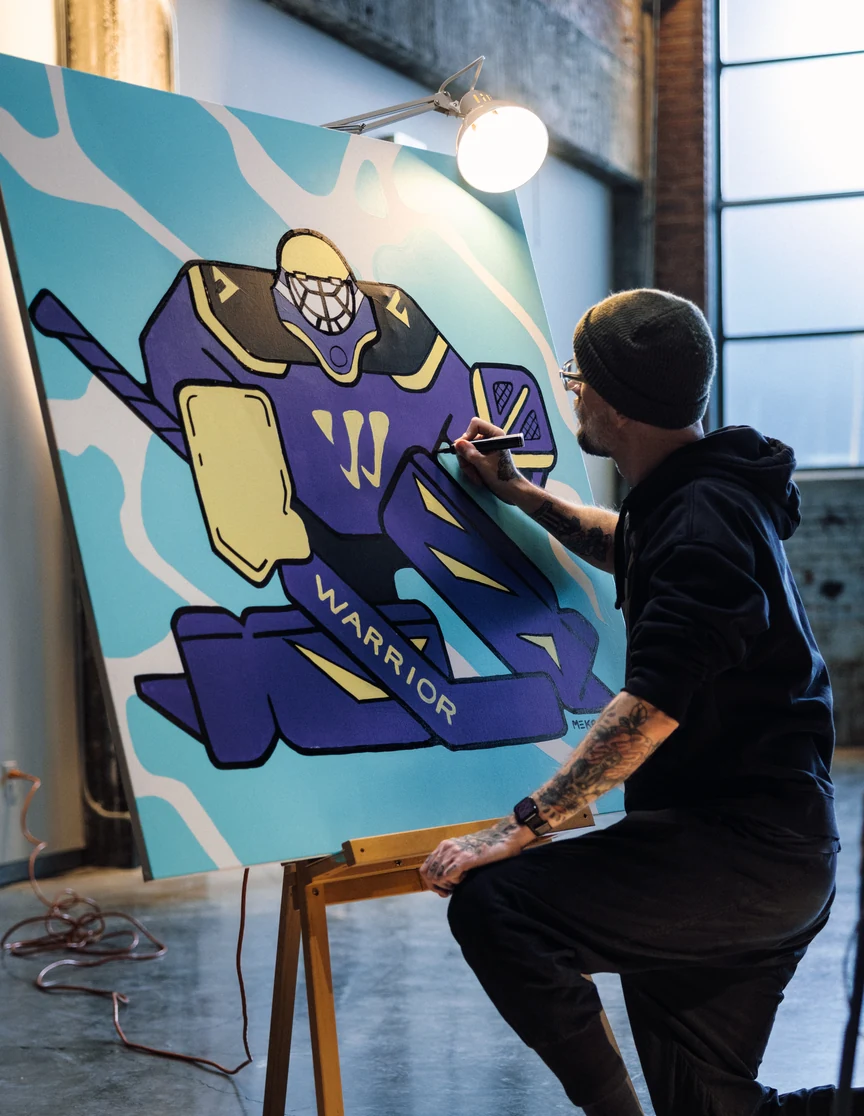 Close on the canvas mid-paint: the goalie in purple and yellow, the artist working the edge of the mark